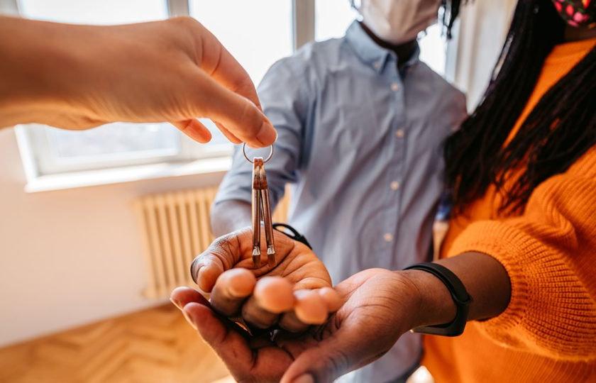 新冠肺炎大流行期间，戴着口罩的年轻夫妇从房地产中介手中接过新房钥匙.
